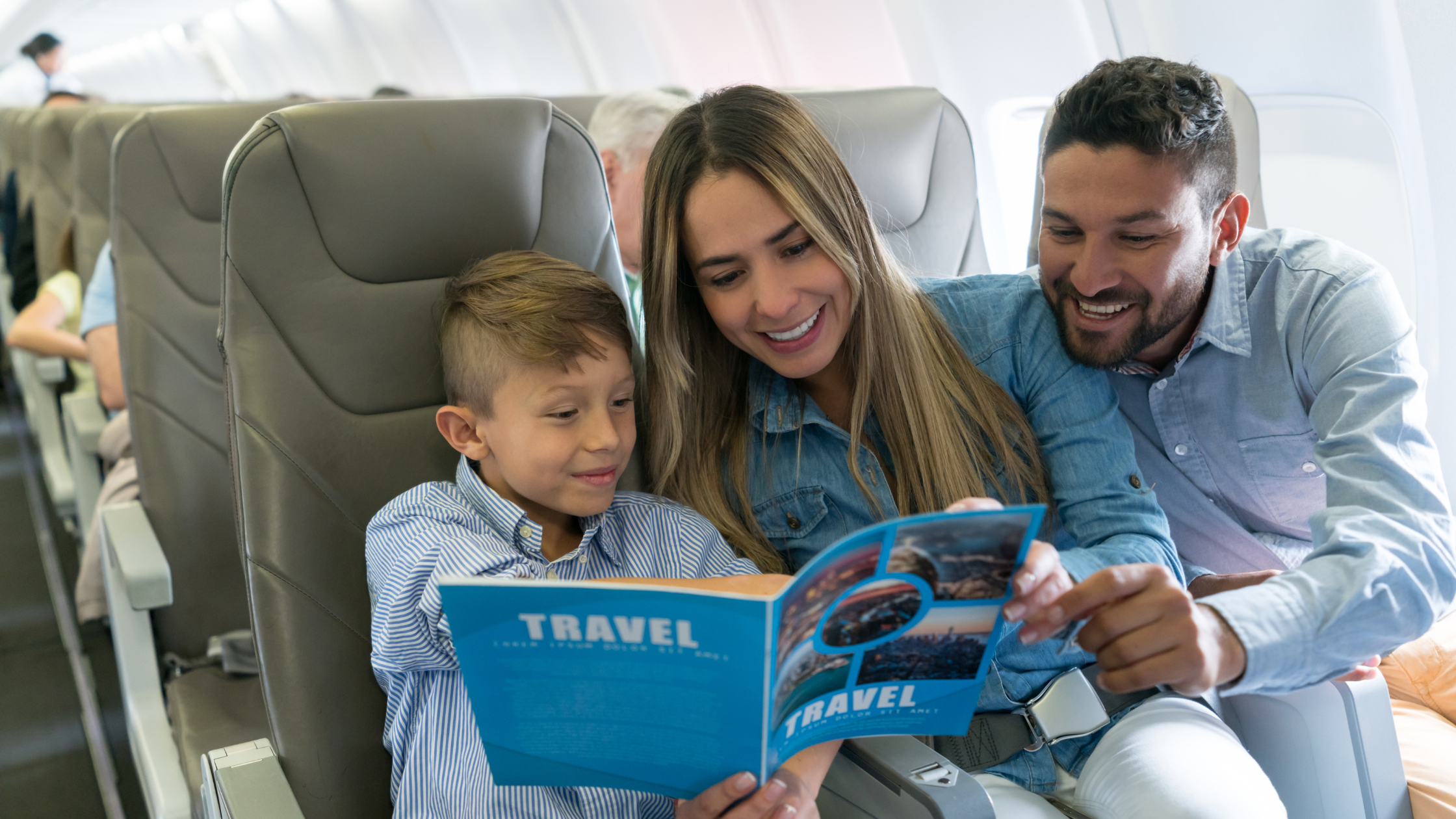 man, woman and child on airplane holding a travel magazine and smiling